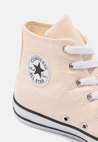 Rosa kanvas høyhælte sneakers med hvite snørebånd, svart gummisåle og en sirkulær logo-patch med en svart stjerne og merkenavn.