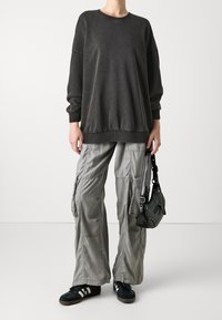 Sudadera gris de gran tamaño con puños y dobladillo acanalados, combinada con pantalones cargo gris claro que cuentan con bolsillos laterales, y bolso de hombro negro.