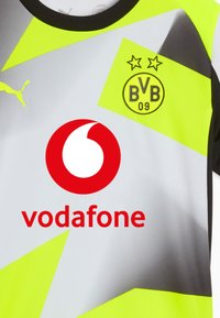 Camiseta de fútbol de Puma con un fondo gris, acentos en amarillo brillante, logotipo de Vodafone en rojo y emblema de BVB 09 con dos estrellas.