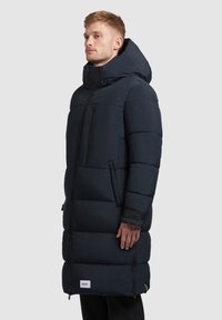 Padded námornícky dlhý kabát s veľkou kapucňou, predným zipsom, bočnými vreckami a elastickými manžetami; obsahuje logo nášivku na dolnej prednej časti.