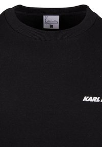 Black sweatshirt with ribbed crew neck, featuring a white “KARL” logo. Soft cotton material, smooth texture, and medium thickness. Size label visible.