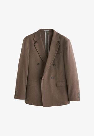 Mann in braunem zweireihigem Blazer passt die Manschette an und zeigt dunkle Knöpfe sowie strukturierten Stoff vor neutralem Hintergrund.