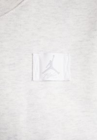 Lys grå sweatshirtstoff med en hvit merkelapp som har en grå Jumpman-logo og "Flight"-tekst. Materialet har en myk, strukturert overflate.
