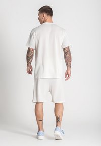 Hellgrauer, gerippter Kurzarm-Top und passende Shorts. Lässige Passform, strukturierte Stoff, mit sichtbaren Tattoos und hellblauen Sneakers.