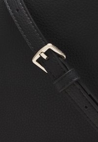 Černý kožený opasek s texturovaným povrchem. Má zlatou kovovou sponu obdélníkového tvaru s hrotem, která je zajištěna skrz zářez.