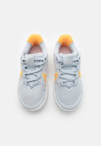 Baskets de sport gris clair avec une tige en tissu texturé, accents orange et un col rembourré. Comprend des lacets et une semelle en caoutchouc.