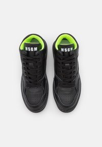 Baskets en cuir noir avec doublure vert néon, bout rond, détails perforés, lacets plats noirs, logo sur la languette, texture de semelle contrastée.