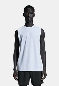 Weißes ärmelloses T-Shirt aus glattem Baumwollstoff, mit rundem Halsausschnitt und lockerer Passform, kombiniert mit dunklen Shorts.