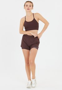 Soutien-gorge de sport marron avec des bretelles fines, associé à un short de sport marron assorti avec une taille élastique, un tissu doux et une coupe décontractée.