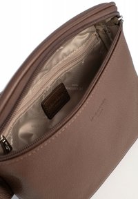 Interieur van een bruine leren tas met een gladde, beige voering. Bevat een ritsvak en een klein leren label met de merknaam in reliëf.