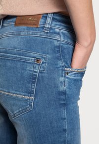 Jeans in denim blu con una finitura sbiadita, dotati di un'etichetta del marchio in pelle marrone, impunture sulle tasche posteriori e rivetti sulle tasche.