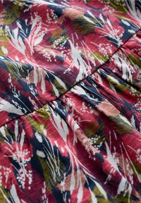 Tkanina w kwiatowy wzór w odcieniach czerwieni, granatu, zieleni i bieli. Miękka w dotyku, z marszczeniami i lekko spływającym układem.