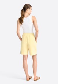 White tank top with a round neckline paired with yellow shorts featuring an elastic waistband and side pockets, shown from the back.