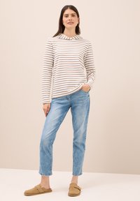 Sudadera de manga larga a rayas en crema y marrón, combinada con jeans de color azul claro y zapatos de esloro marrones, exhibida sobre un fondo neutro.