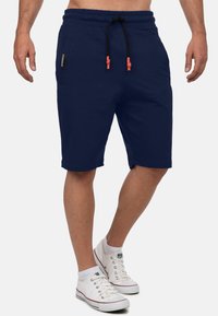 Marineblauwe katoenen shorts met een elastische tailleband, zwarte trekkoord en twee zakken. Gecombineerd met witte sneakers en enkel-sokken.