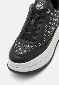 Sneaker in pelle nera con occhielli argentati, lacci neri e una spessa suola piattaforma bianca con un fondo nero a contrasto.