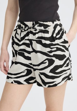 Femme portant un short imprimé zèbre noir et blanc avec une taille élastique et un cordon, associé à un haut noir sans manches.