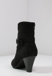 Bota de ante negra hasta el tobillo con un tacón afilado, que cuenta con una correa decorativa con hebilla alrededor del tobillo y un acabado liso.