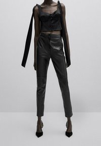 Black satin cropped top with button detail and long straps, paired with high-waisted black faux leather pants, complemented by pointed heels.