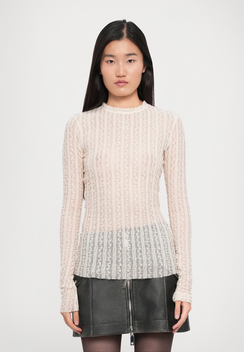 Top trasparente a maniche lunghe con motivo in pizzo floreale, di colore rosa chiaro e design aderente. Abbinato a una gonna scura con zip.