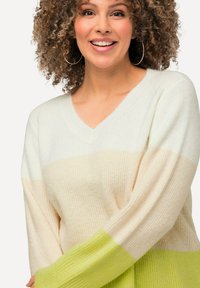 V-ringad tröja med avslappnad passform, med horisontella ränder i krämfärg, persika och klargrön. Mjuk stickad textur och långa ärmar.