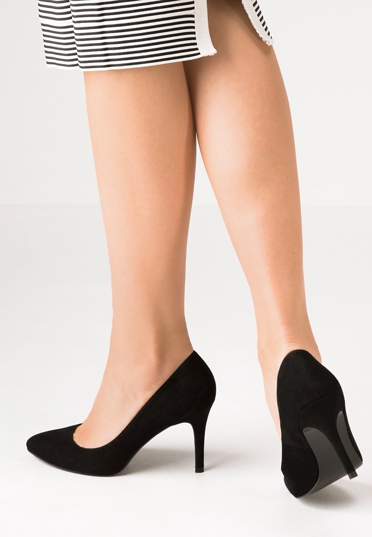 Chaussures à talons hauts en daim noir avec un bout pointu et un talon aiguille fin, présentées sur un fond neutre.