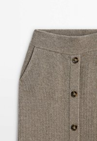 Jupe grise tricotée avec taille côtelée, poches latérales et trois boutons marron au centre devant sur fond blanc.