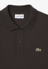 Tummanruskea slim fit Lacoste-paita, jossa on kaulus, kaksi mustaa nappia ja vihreä krokotiililogo rinnassa.