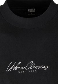 Fekete pamut póló, kerek nyakkal, rövid ujjakkal és fehér hímzett felirattal: "Urban Classics EST. 2005" az elején.