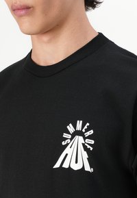 Zwarte katoenen t-shirt met een wit grafisch logo en de tekst "SUMMER OF HUF", ronde hals en korte mouwen. Gladde textuur, casual pasvorm.