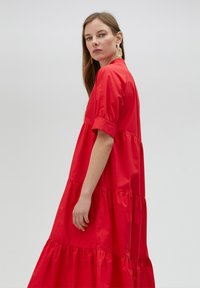 Robe en coton rouge avec des manches courtes, design à volants superposés et coupe décontractée. Texture lisse, longueur mi-mollet.