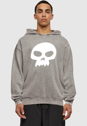 Felpa grigia oversize con una texture morbida, caratterizzata da una grande grafica di teschio bianco sulla parte anteriore e un cappuccio con cordino.