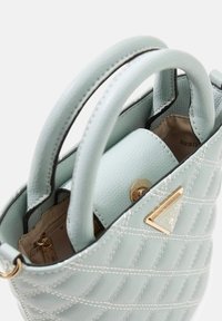 Lichtblauwe leren handtas met een gewatteerd ontwerp, afgeronde bovenhandvatten en gouden hardware accenten. Binnenkant bevat een ritsvak.