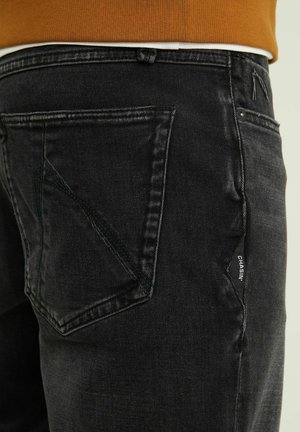 Černé džíny z denimu s úzkým střihem, které disponují výrazným designem zadní kapsy a jemnými švy. Visačka viditelná na bočním švu.
