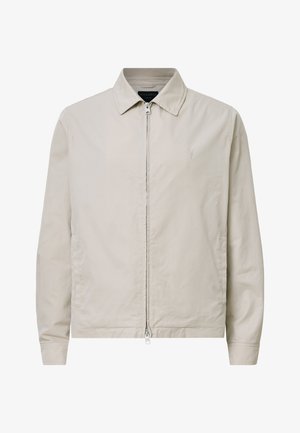 Giacca zip-up beige chiaro con colletto a punta, maniche lunghe e un logo sottile sul lato sinistro del petto. Texture liscia e design minimal.