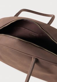 Saco de couro castanho com uma textura suave e duas alças superiores. Apresenta um fecho de correr em tom dourado e um interior espaçoso. Design minimalista.