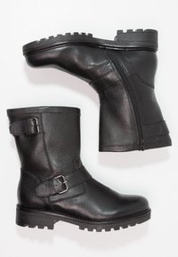 Botas de tobillo de cuero negro con un acabado texturizado, cremallera lateral y detalles de hebilla ajustable. Suela de goma resistente con un diseño con relieve.