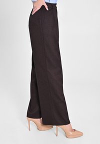 Braune, weite Hosen aus strukturiertem Stoff mit hoher Taille, Seitentaschen und einem goldenen Knopfdetail, kombiniert mit nudefarbenen High Heels.