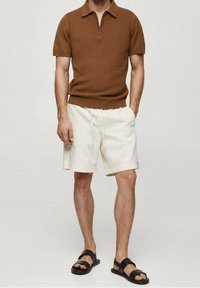 Brown short-sleeve knitted polo shirt with zip; paired with white drawstring shorts and black flat sandals. Neutral colors and relaxed fit.