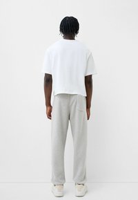 Weißes, kurzes T-Shirt, lockere Passform, kombiniert mit hellgrauen Jogginghosen, weiche Textur, schlichtes Design, Seitentaschendetail, lässiges Schuhwerk.