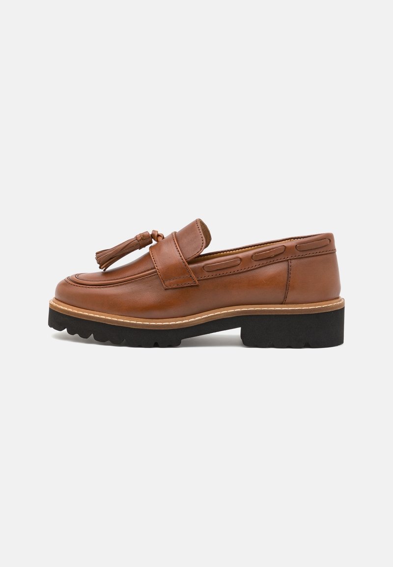 Mocassin à pampilles en cuir marron avec semelle noire épaisse et détails cousus, vu de côté sur un fond uni.