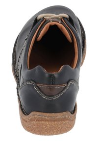 Zapato negro de piel sin cordones con punta redonda, interior de color tostado y suela de corcho texturizada. Detalle de costura a lo largo de los lados y el talón.