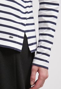 Långärmad skjorta i vitt och marinrandigt, i bomullstyg, med sidofickor och en metallisk logotagg nära fållen.