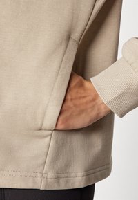 Lichtbeige sweatvest met een gladde textuur, voorzien van een zijzak en geribbelde manchetten. Eenvoudig ontwerp met minimale stikseldetails.