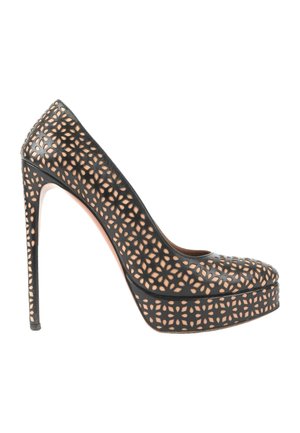Zapato salón negro de tacón alto con plataforma y un diseño floral recortado que revela el forro de color nude debajo.