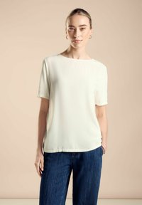 Lehký, krémový top s krátkými rukávy, rovného střihu a kulatým výstřihem, doplněný o tmavě modré kalhoty širokého střihu.