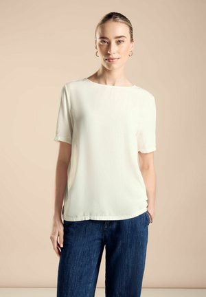 Top leggero color crema con maniche corte, taglio dritto e scollatura rotonda, abbinato a jeans a gamba larga blu scuro.