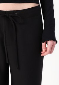Black sweatpants made from soft material, featuring a drawstring waist, and a ribbed long-sleeve top with scalloped cuffs.