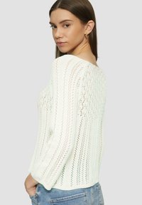 Weißer Strickpullover mit lockerer Passform, rundem Ausschnitt und verlängerten Ärmeln, die ein strukturiertes, offenes Strickdesign aufweisen.