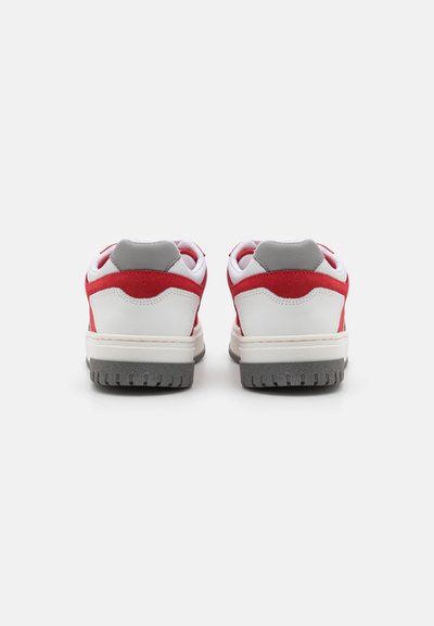 Zapatillas deportivas rojas y blancas con acentos grises; materiales de cuero suave y gamuza; diseño de bajo perfil con una suela exterior de goma texturizada.